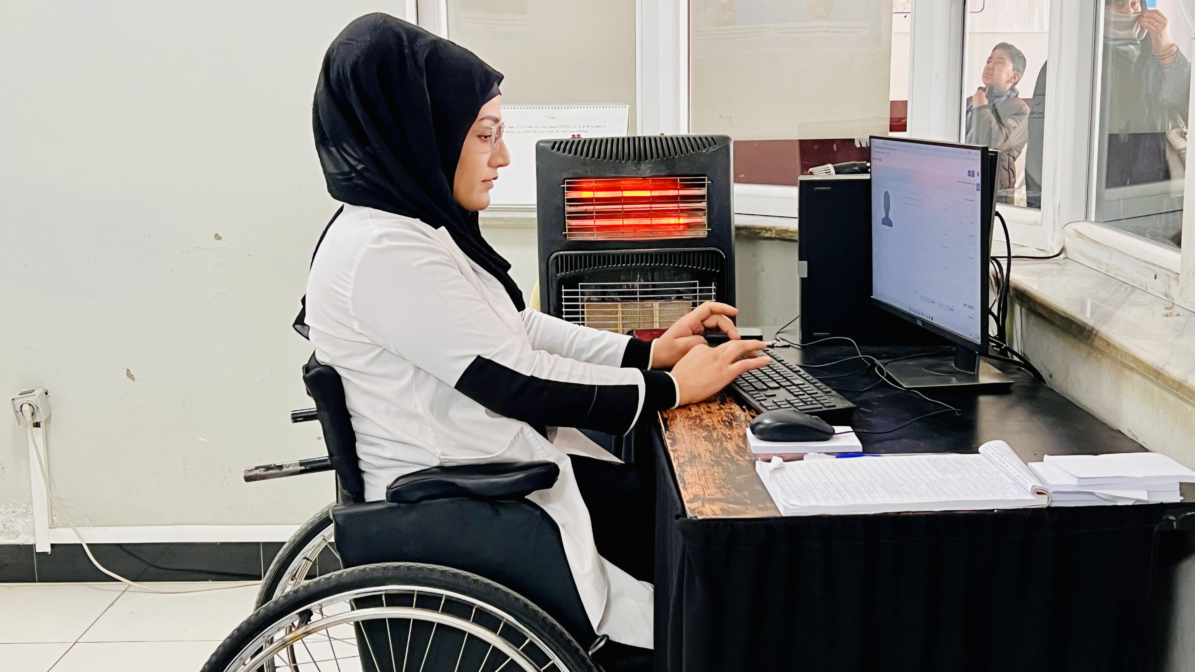A woman in a wheelchair types in front of a computer in Afghanistan.