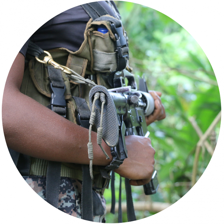 Torso de una persona con vestimenta militar empuñando un arma en reposo.