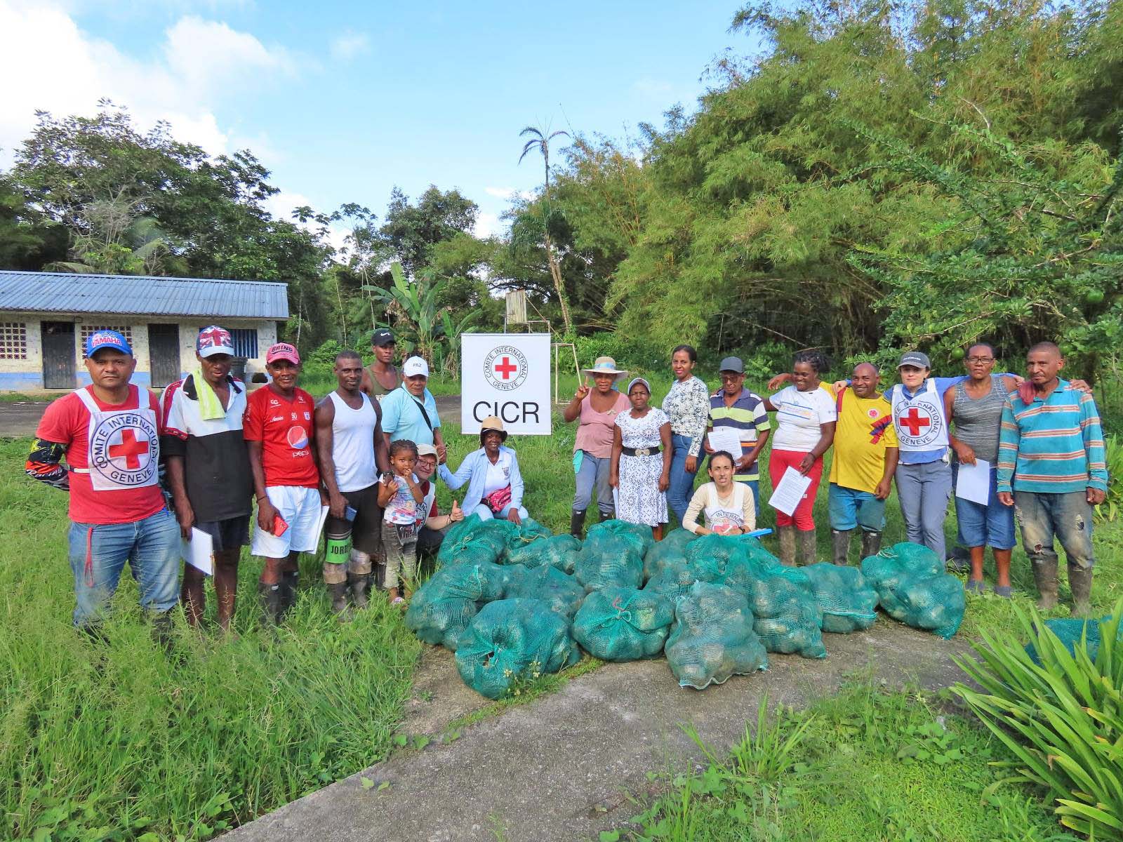 Un grupo de personas está alrededor de unas bolsas que contienen semillas de plátano, mientras posan a la cámara.