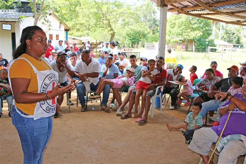 Una persona del CICR se dirige a una comunidad. De fondo se ven varias personas sentadas y prestando atención a la charla.