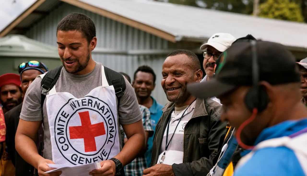 An ICRC staff member and the head teacher hand out school supplies to students.
