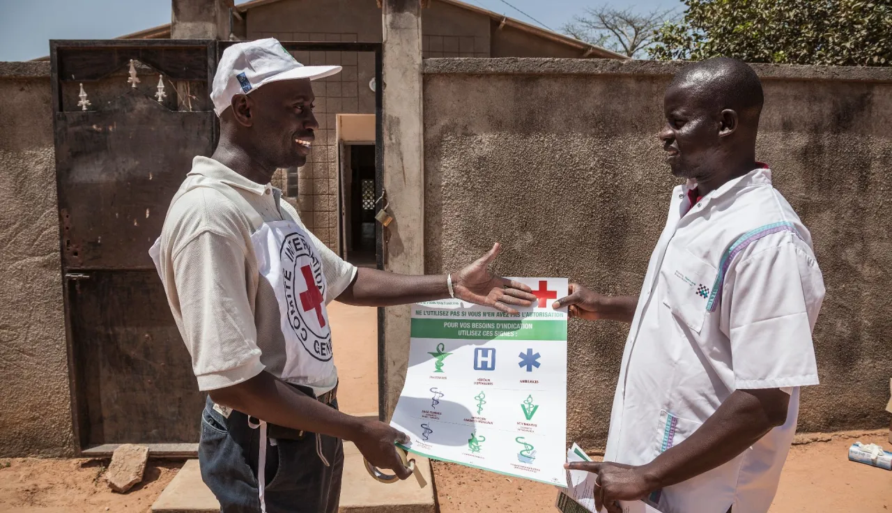 An ICRC staff provides a poster with various logos to a head nurse