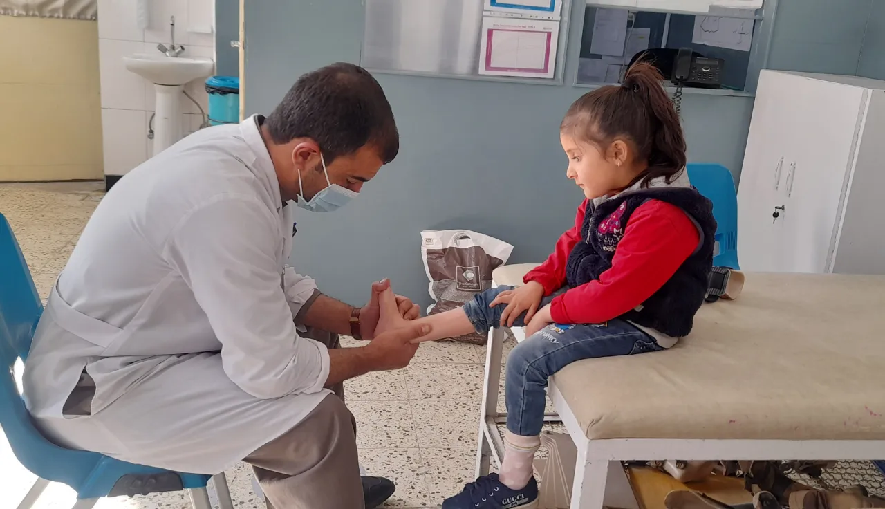 An ICRC doctor checking the ankle of a child seated on an examination table, in Afghanistan.