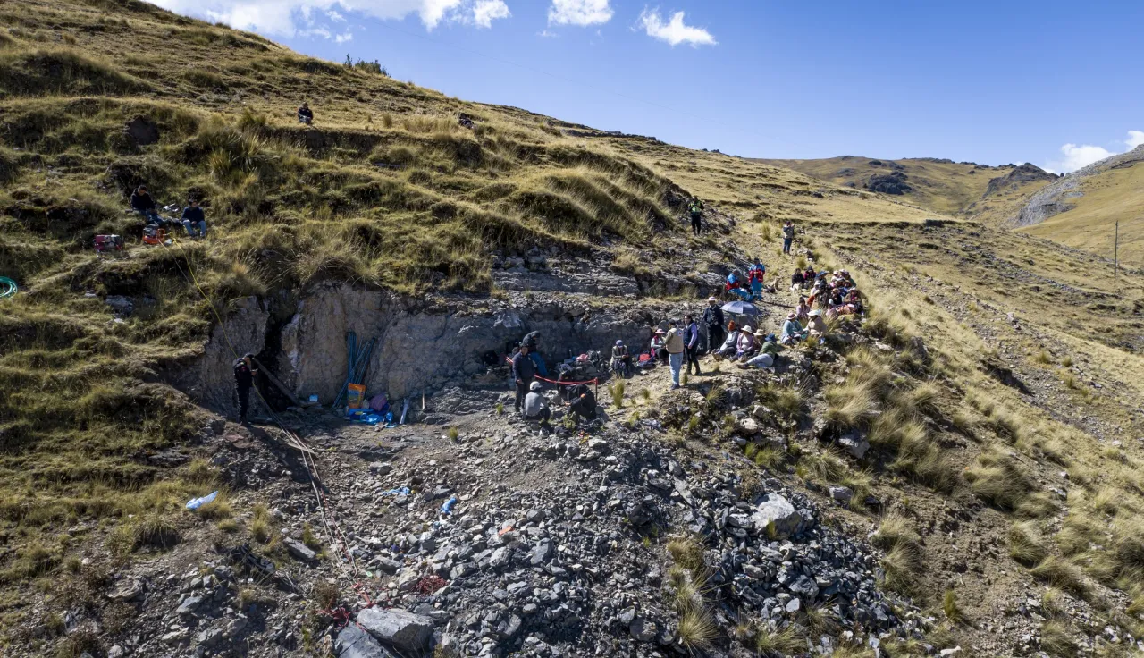 Foto: Jesús Moya Choy/CICR Toma aérea de una fosa en medio de una montaña, con personas presenciando detrás de un cordon de seguridad.