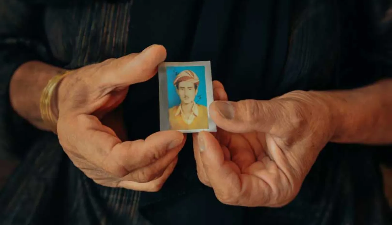 A woman in iraq holds a passport sized photograph of a missing relative