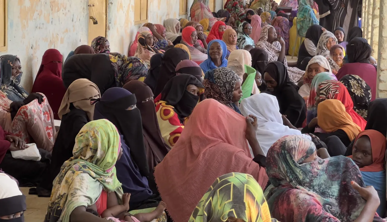 Sudanese women sitting by the wall of a school.