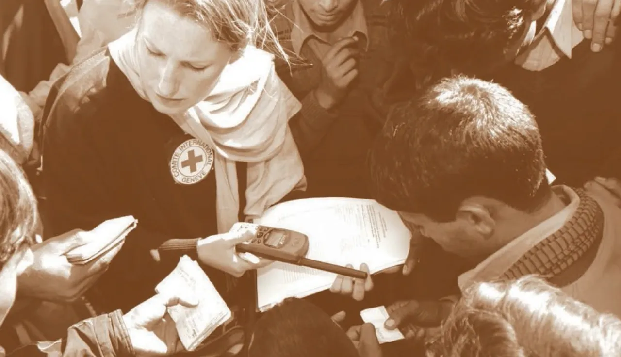 Funcionária do CICV, com uma lista e um rádio na mão, verifica documentos de pessoas.