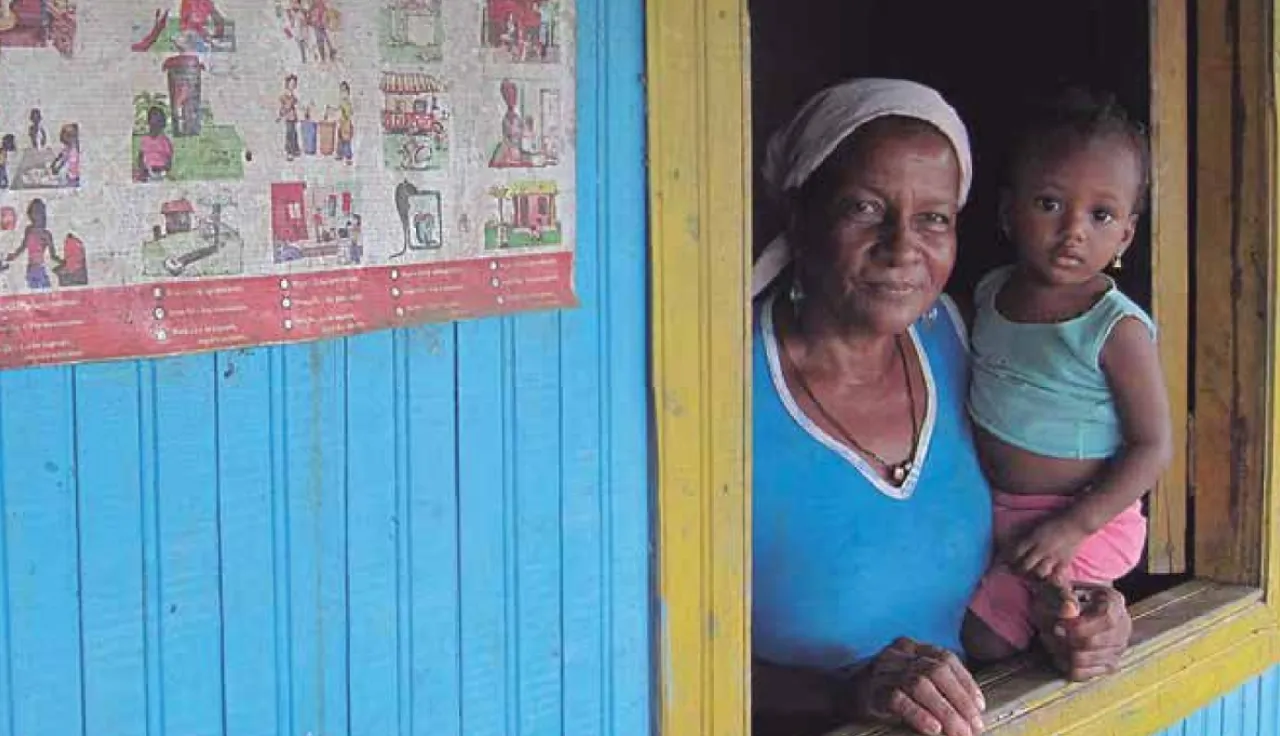 Una mujer con su hijo en brazo miran por la ventana de su hogar en Colombia.