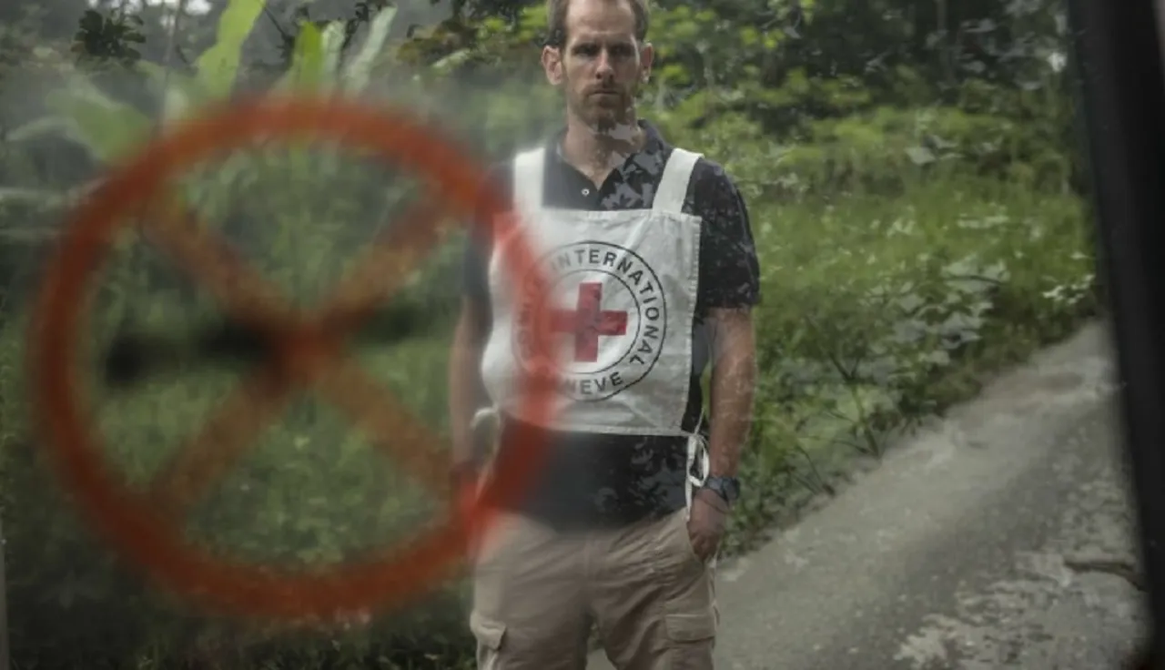 Un delegado del CICR con un fondo selvático en Colombia. En primer plano se ve un símbolo de prohibido el uso de armas de fuego.