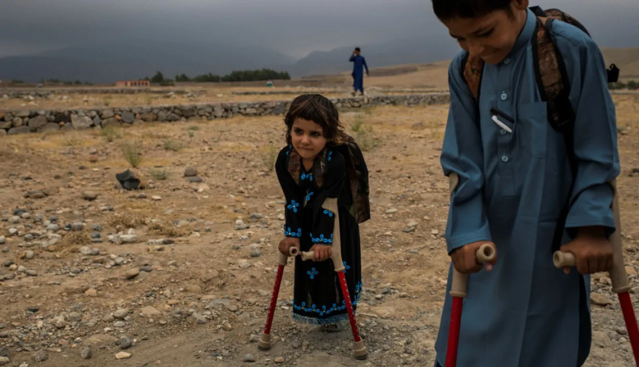 Duas crianças andam de muletas num terreno desértico.