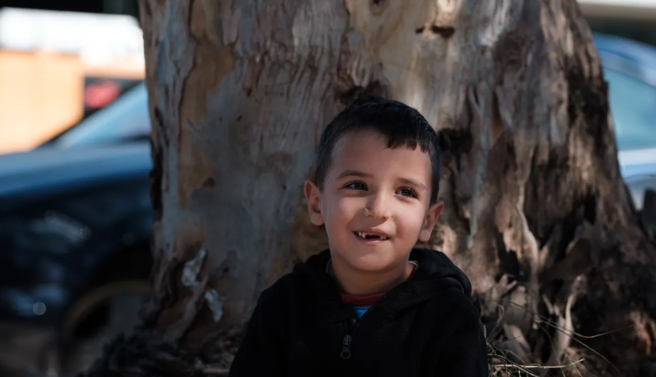 A child sits by a tree