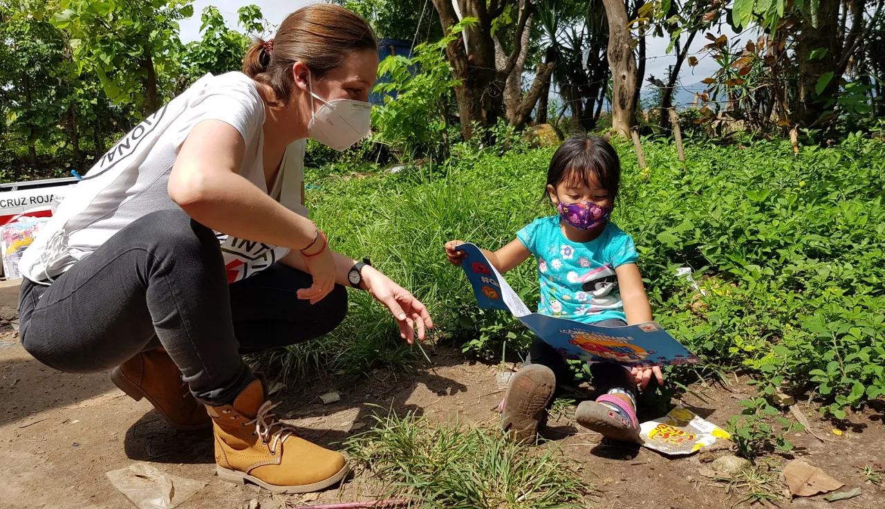 Una delegada del CICR dialoga con una niña pequeña que lee un folleto del CICR sobre el COVID-19, en un entorno rural.