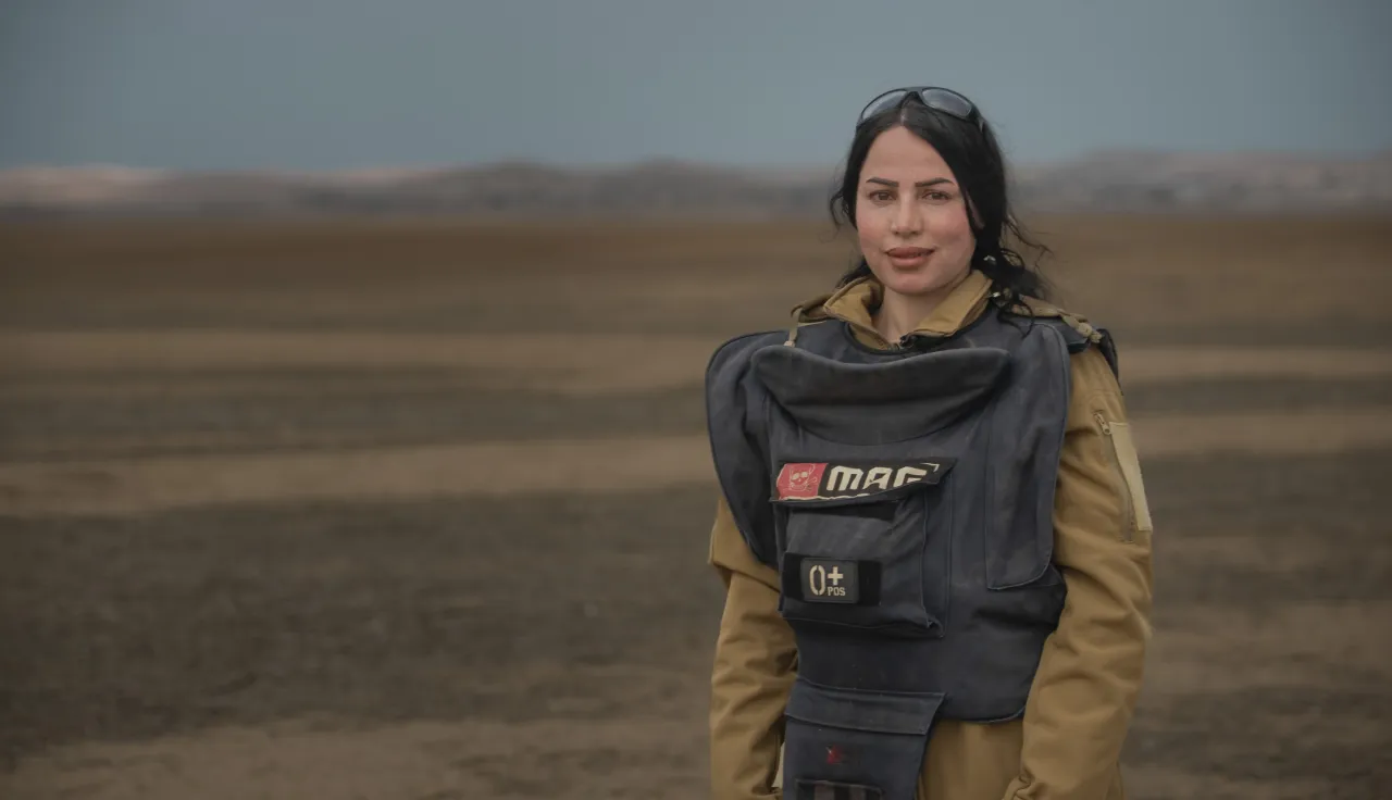 Noora Murad wearing protective gear looks at the camera from a mine field in Iraq.