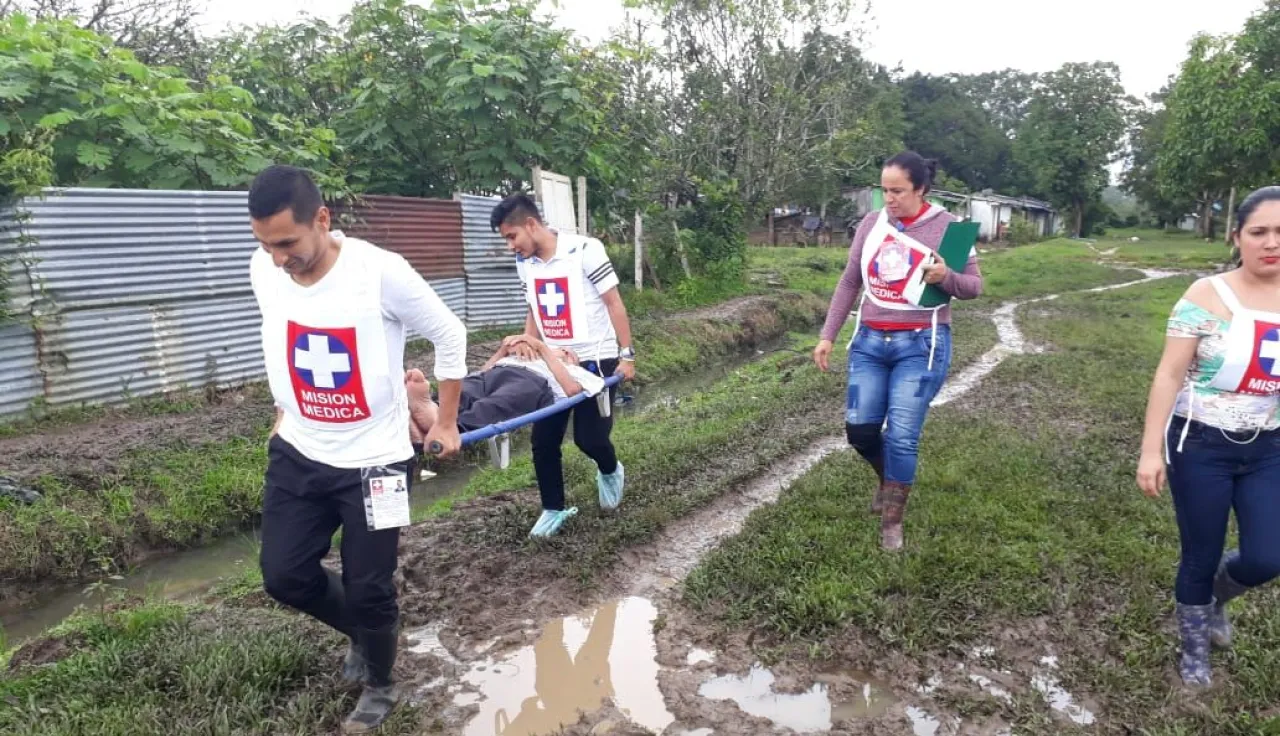 Dos personas de la misión médica llevan a un paciente, mientras otras personas, también de la misión médica, acompañan el proceso