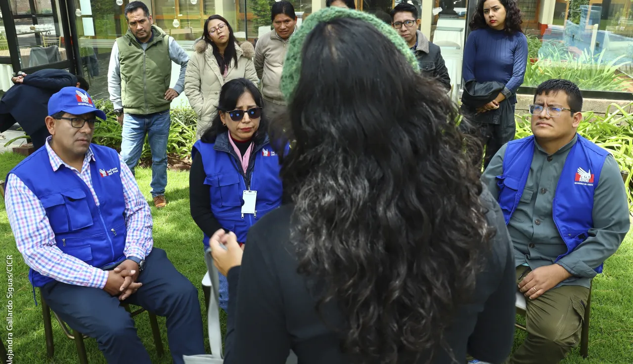 Trabajadores de la Defensoría del Pueblo observan a una mujer que aparece de espaldas en la foto.
