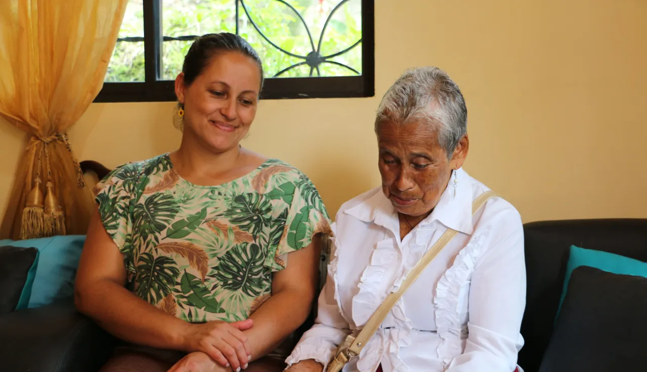 Una mujer mira una fotografía de una manera emotiva, mientras otra persona la acompaña, mientras sonrie y mira la foto también
