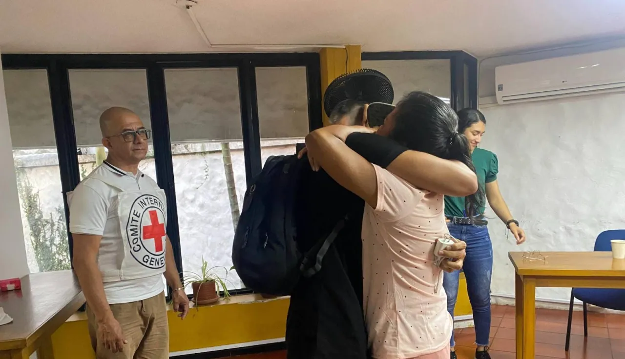 Dos personas se abrazan, mientras otras dos personas presencian el momento de reencuentro