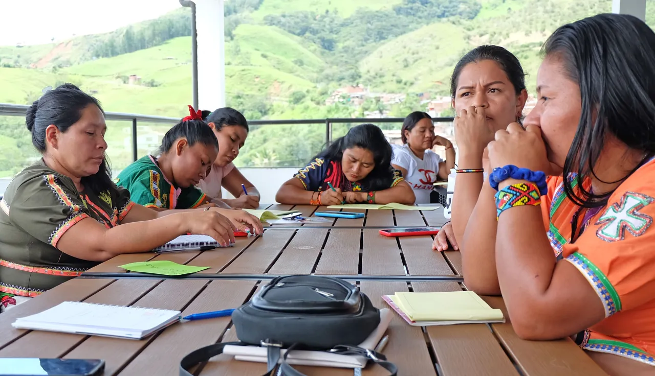 Siete mujeres están sentadas en una mesa, escribiendo y reflexionando
