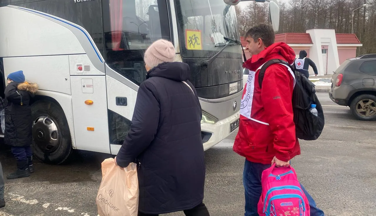 Сотрудник МККК сопровождает женщину с вещами к автобусу. 