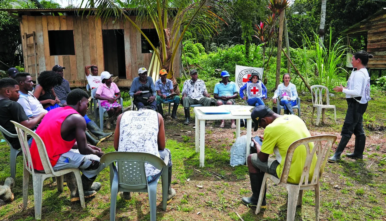Una persona del CICR está dando una charla a un grupo de personas de una comunidad. Están al aire libre, sentados haciendo un círculo.