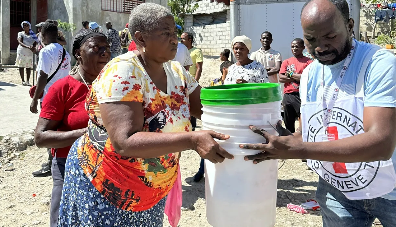 An ICRC staff helps a woman in Haiti to carry some buckets.
