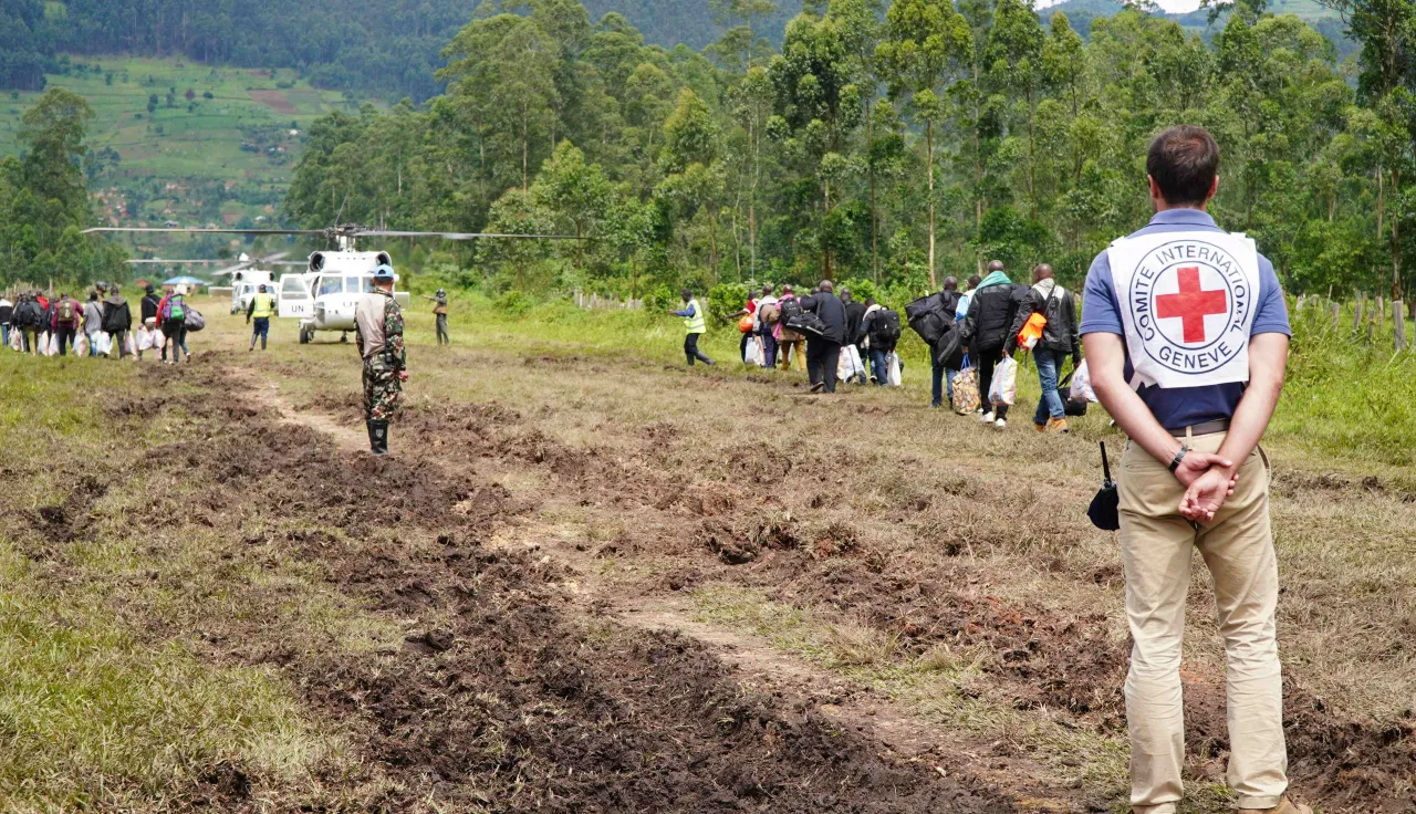 DRC operation ICRC staff member in the foreground on a dirt road, with people walking towards an aeroplane in the background