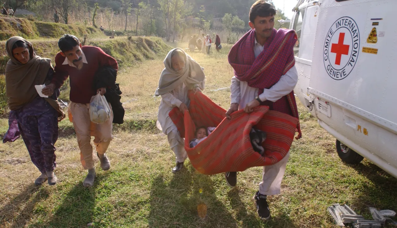 People carry a patient wrapped in a blanket to an ICRC helicopter for a medical evacuation from Saidpur to Muzaffarabad, Pakistan.