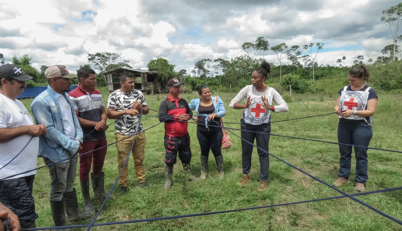 Habitantes de una zona rural participan en una actividad colectiva, en la que sostienen una cuerda entrelazada que forma una red simbólica. El ejercicio se realiza en compañía de integrantes del CICR.