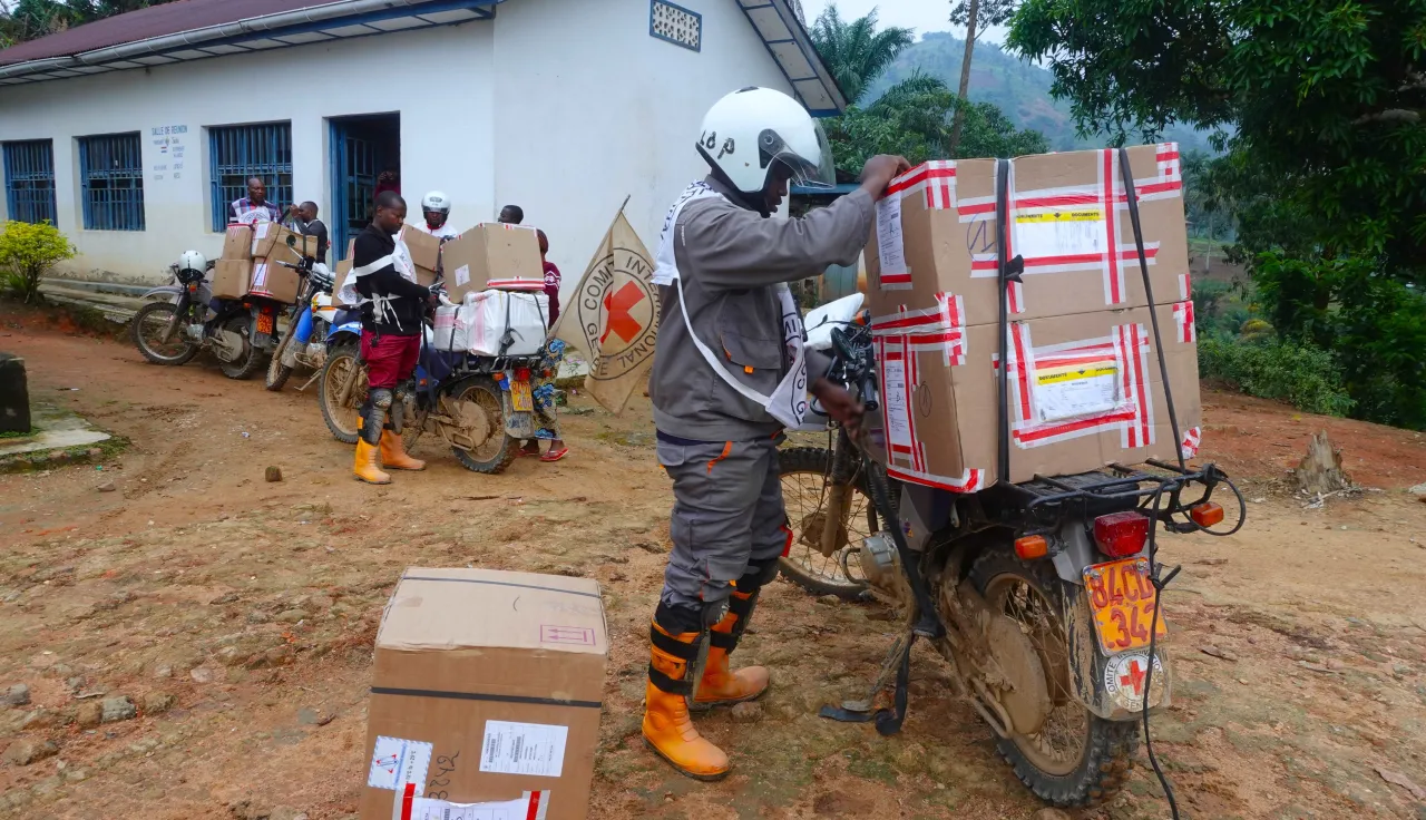 Des travailleurs humanitaires chargent de grandes boîtes de matériel médical sur des motos devant un centre de santé rural, en préparation pour la livraison d’aide dans des zones reculées