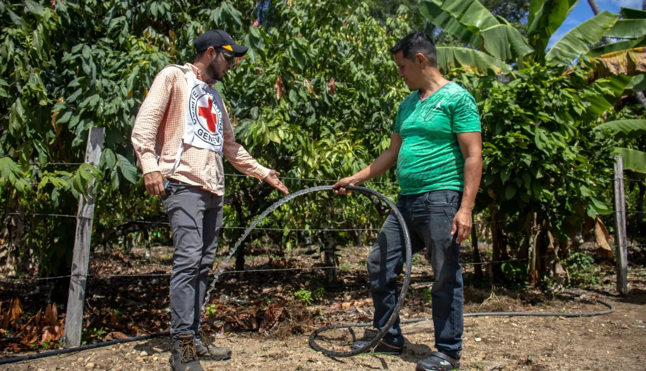 Un señor de la comunidad está junto a un trabajador del CICR. El señor está sosteniendo una mangera de donde sale agua