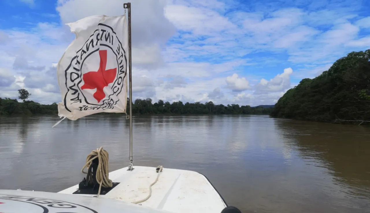 Bandera del CICR en una lancha junto a un paisaje ribereño.