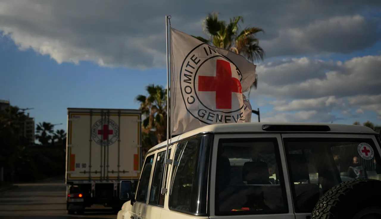 An ICRC vehicle displaying a Red Cross flag follows a truck carrying humanitarian supplies along a coastal road in Lebanon during operations amid escalating hostilities.