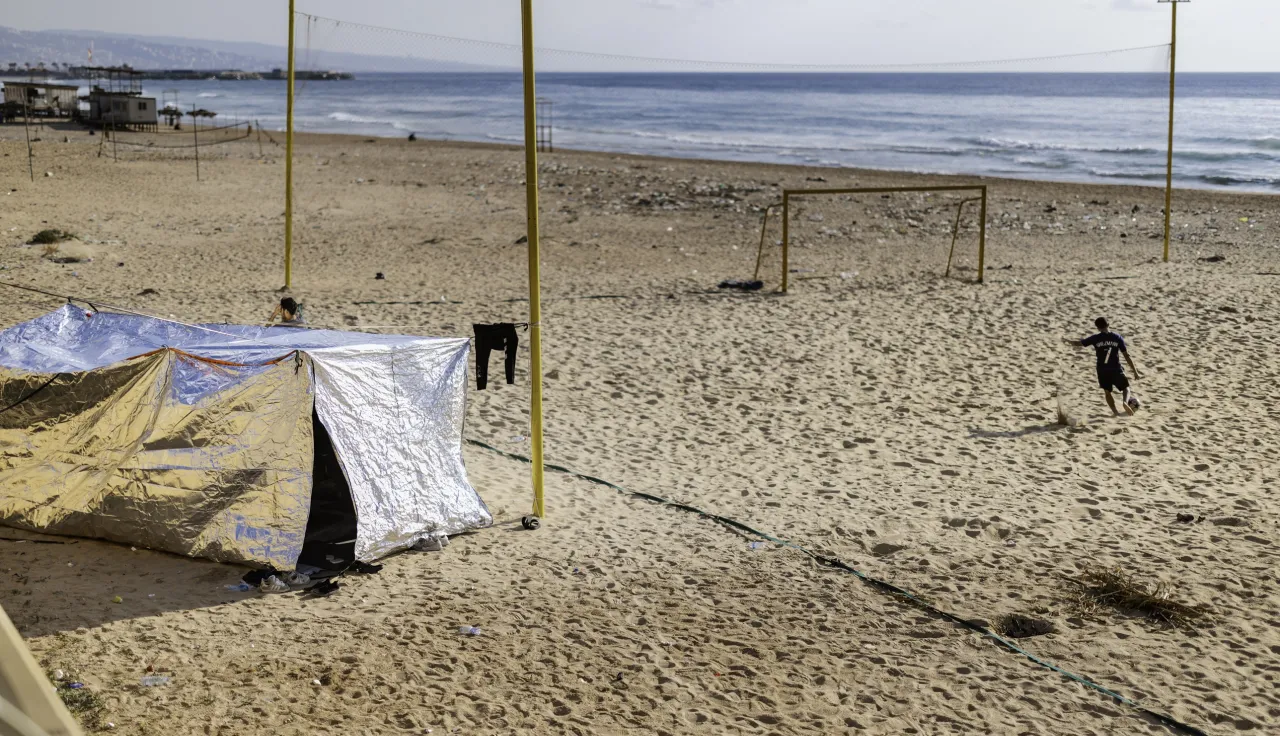 A boy plays football on the beach along the Corniche in Beirut, Lebanon, on March 7, 2026, next to a tent set up by a displaced family who had to move from Beirut’s southern suburbs following an evacuation order issued by Israel.