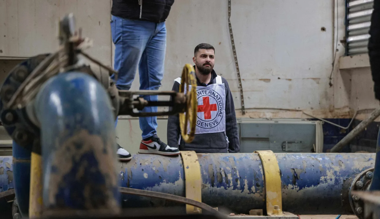 ICRC staff member standing beside large blue water pipes and filtration infrastructure at a water treatment facility in Lebanon, monitoring equipment used to maintain water supply.