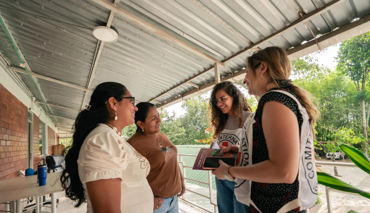 Alt text: Cuatro mujeres conversan en un espacio comunitario. Dos de ellas representan a una comunidad local y las otras dos pertenecen al Comité Internacional de la Cruz Roja. Todas participan activamente en la conversación, mostrando un ambiente de diálogo y colaboración.
