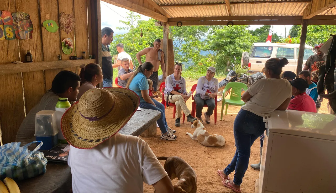 Personas de una comunidad rural en Colombia están sentadas en grupo mientras conversan con representantes del Comité Internacional de la Cruz Roja (CICR), en un entorno comunitario.