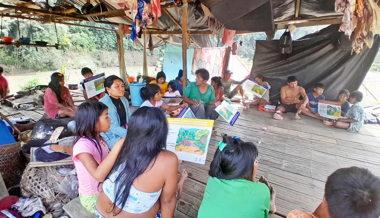 Comunidad indígena en una zona rural de Colombia participa en un taller sobre comportamientos seguros frente a riesgos de artefactos explosivos. Varias personas están sentadas en un salón comunitario, escuchando atentamente una capacitación.