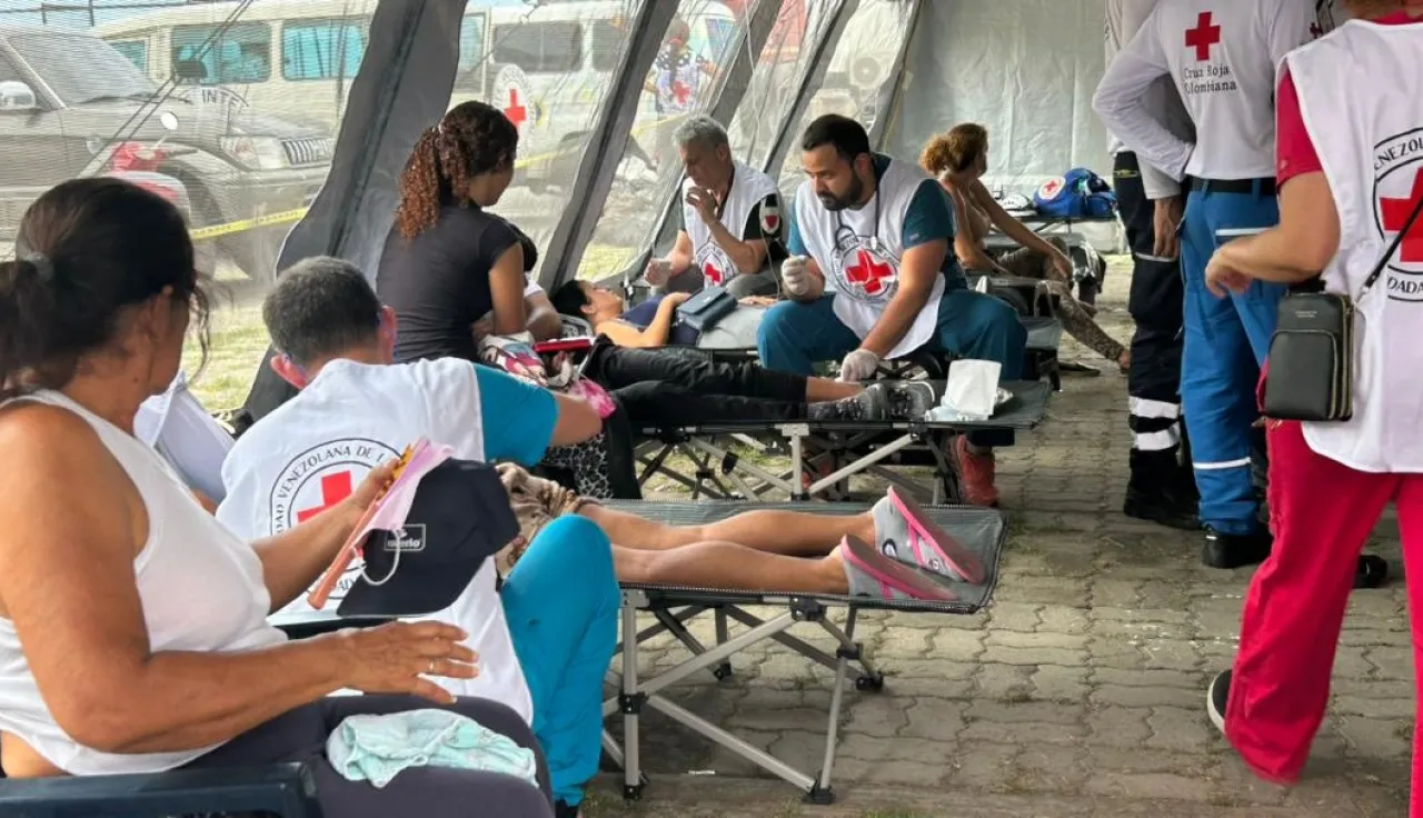 People receive medical care from Venezuelan Red Cross volunteers at a temporary outdoor treatment area following the June 2026 earthquakes in Venezuela. Several patients rest on folding stretchers while volunteers provide first aid and medical assistance.