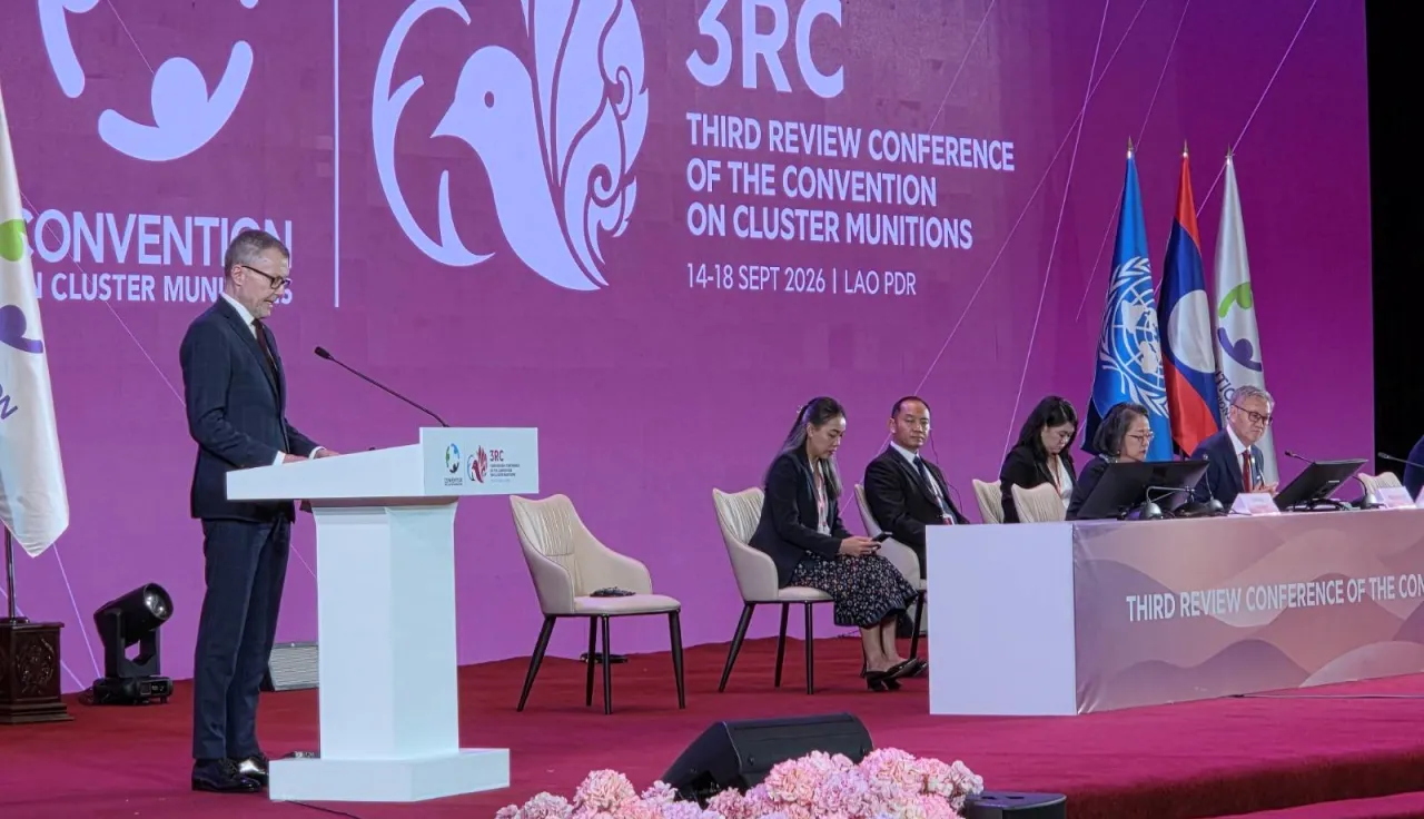 ICRC Vice-President Jürg Lauber speaks at the Third Review Conference of the Convention on Cluster Munitions, with panelists seated on stage and conference branding and flags in the background.