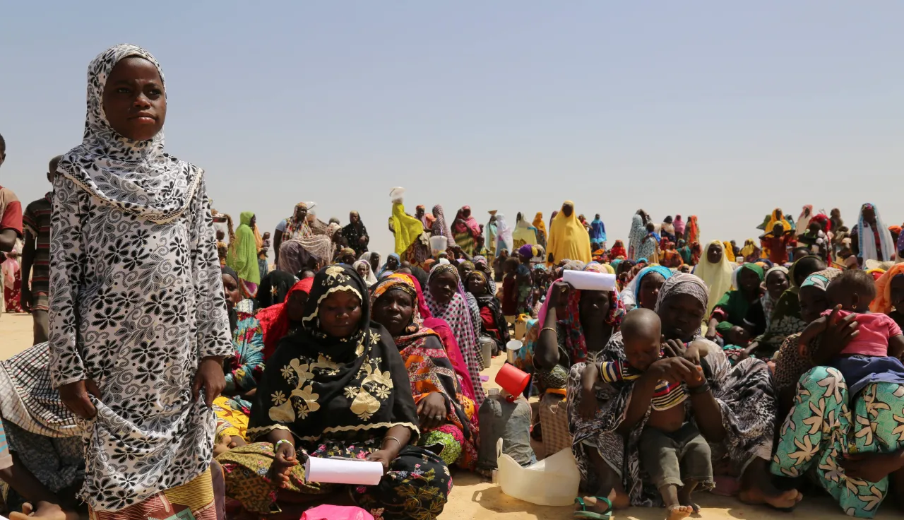 Niger ICRC evaluations A group of people at an ICRC distribution in Niger. Most seated in the sand, one girl is standing in the foreground.
