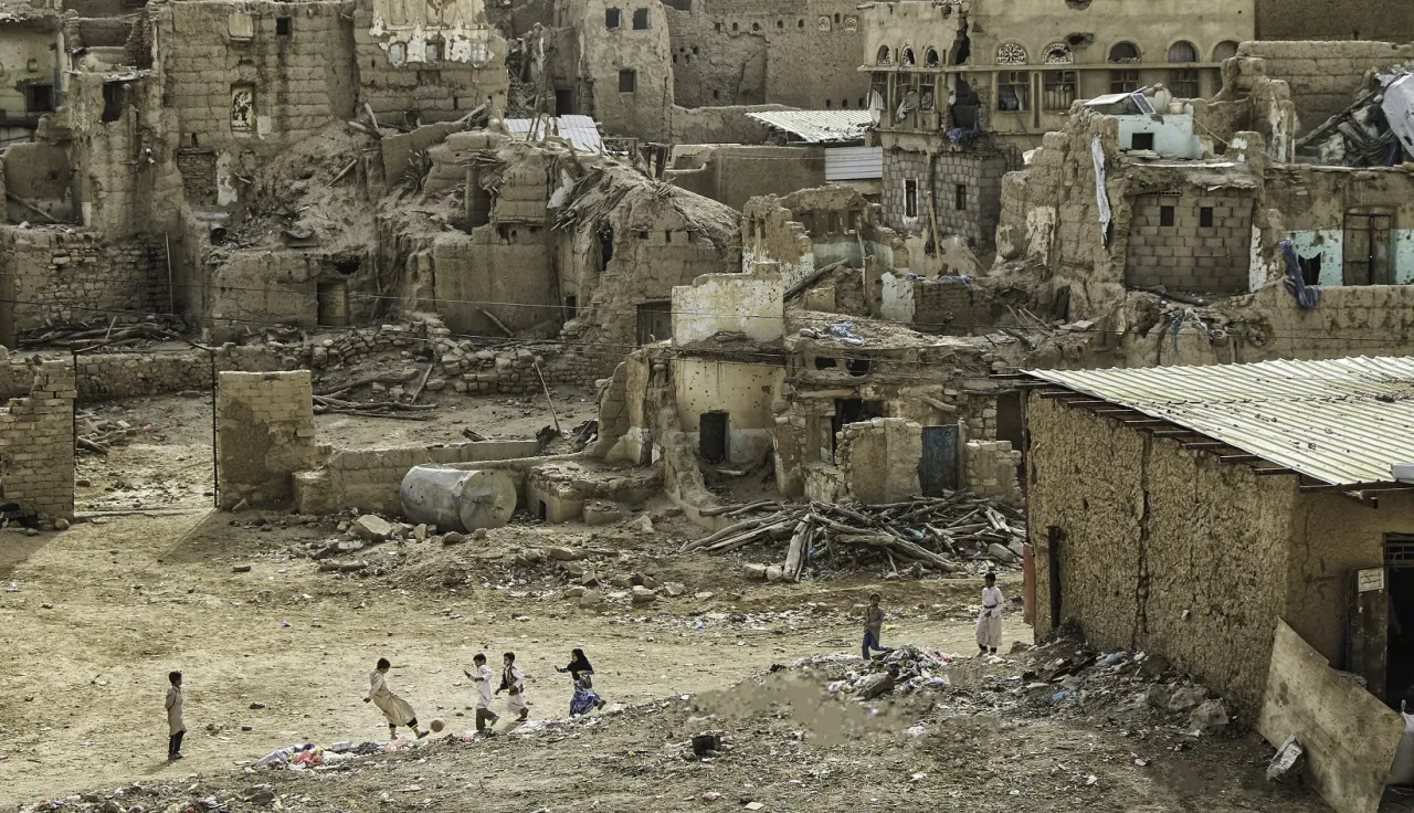 Group of children play football against a backdrop of destroyed houses.