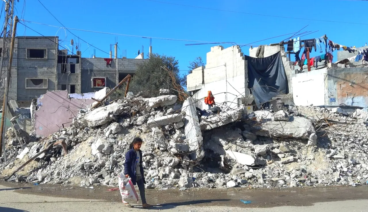 A little girl carrying a bag of supplies walks past destroyed buildings in Rafah, Gaza