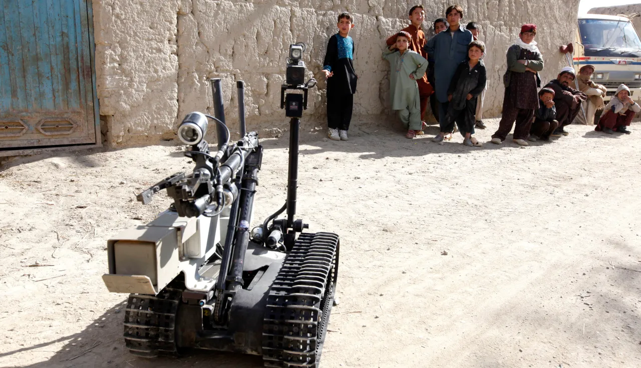 A robot used in war at the foreground while children look on in the background. 