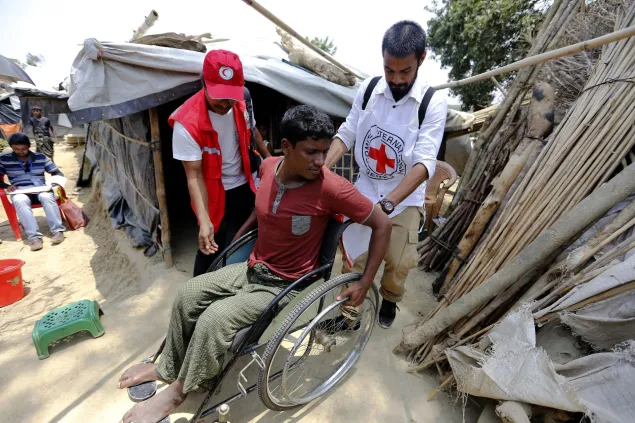 An ICRC field officer and a Bangladesh Red Crescent Society member are assisting a refugee from Myanmar with physical disabilities.