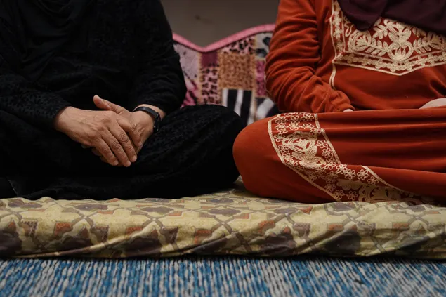 Two women sitting cross-legged on the floor, hands clasped