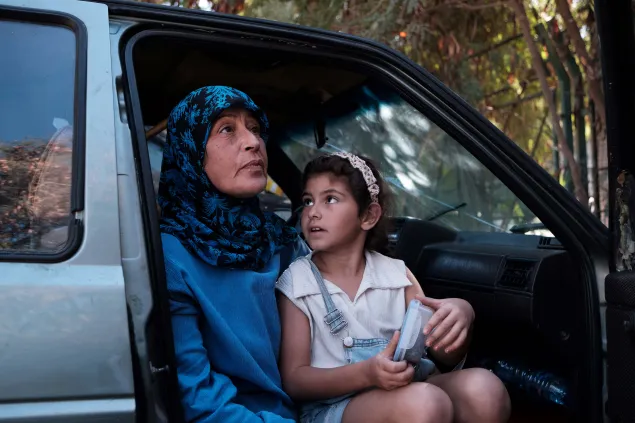 Batoul sits on her mother's lap in a car with an open door