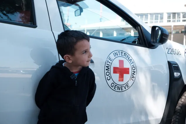 Ghadi leans agains an ICRC vehicle, his face in side profile as he looks at something outside the frame, ICRC logo to his left