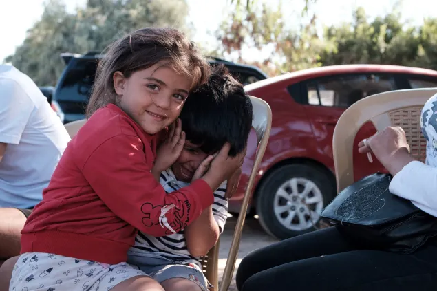 Maria wears a red sweater and holds the face of another child as she smiles for the camera