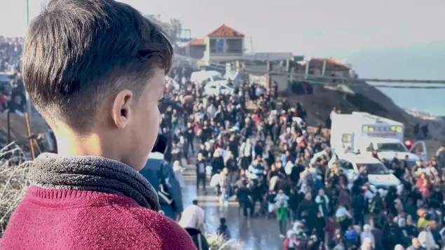 A child observes as crowds of people walk along a road