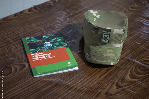 Imagen de un folleto de derecho internacional humanitario junto a una gorra militar.